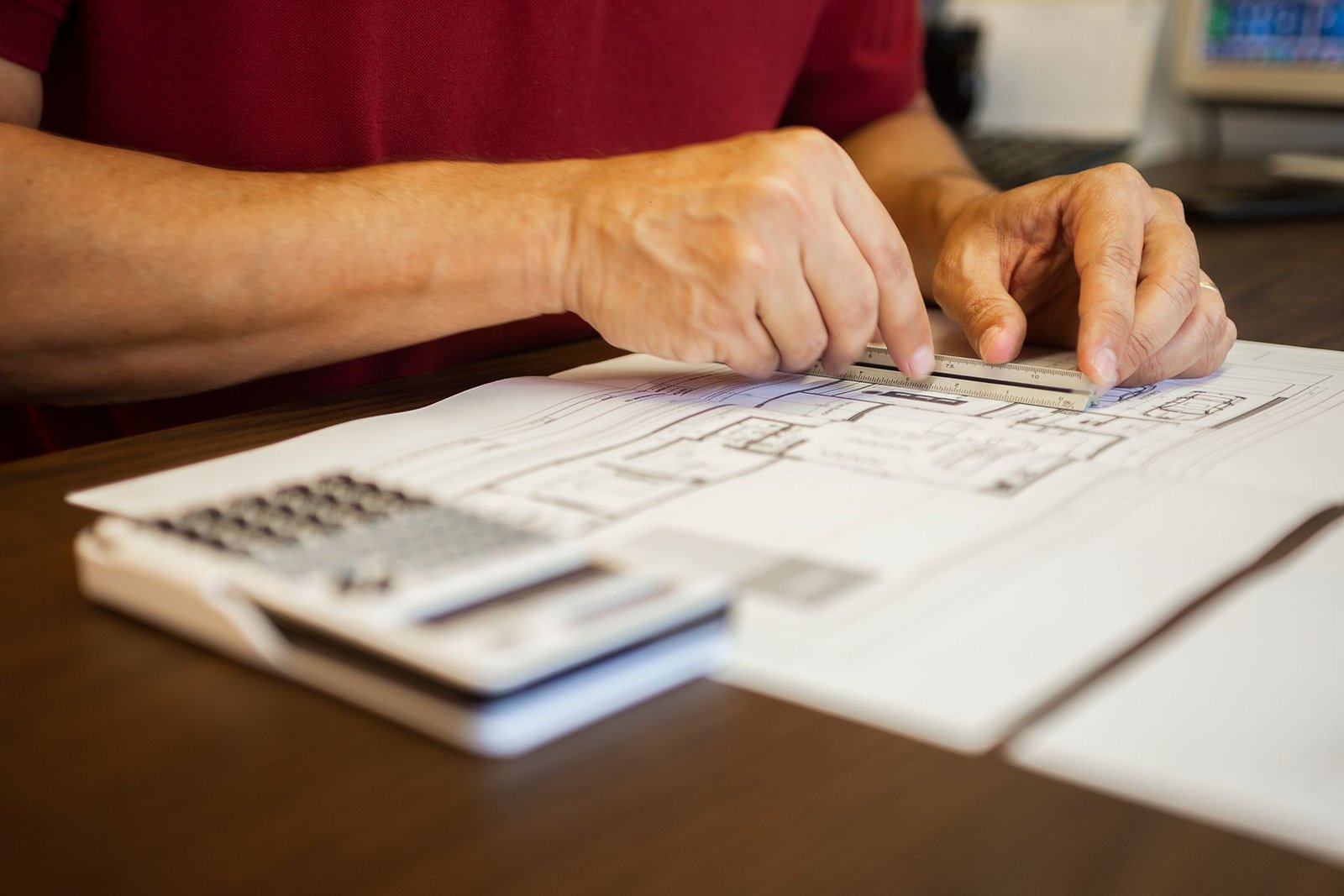 Hands using a ruler on an architectural drawing, with a calculator on the table.