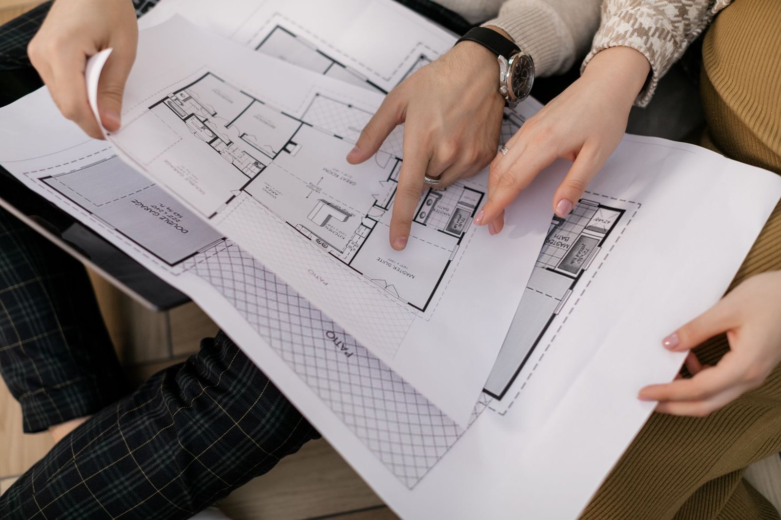 Several hands holding and pointing to details on printed architectural floor plans.