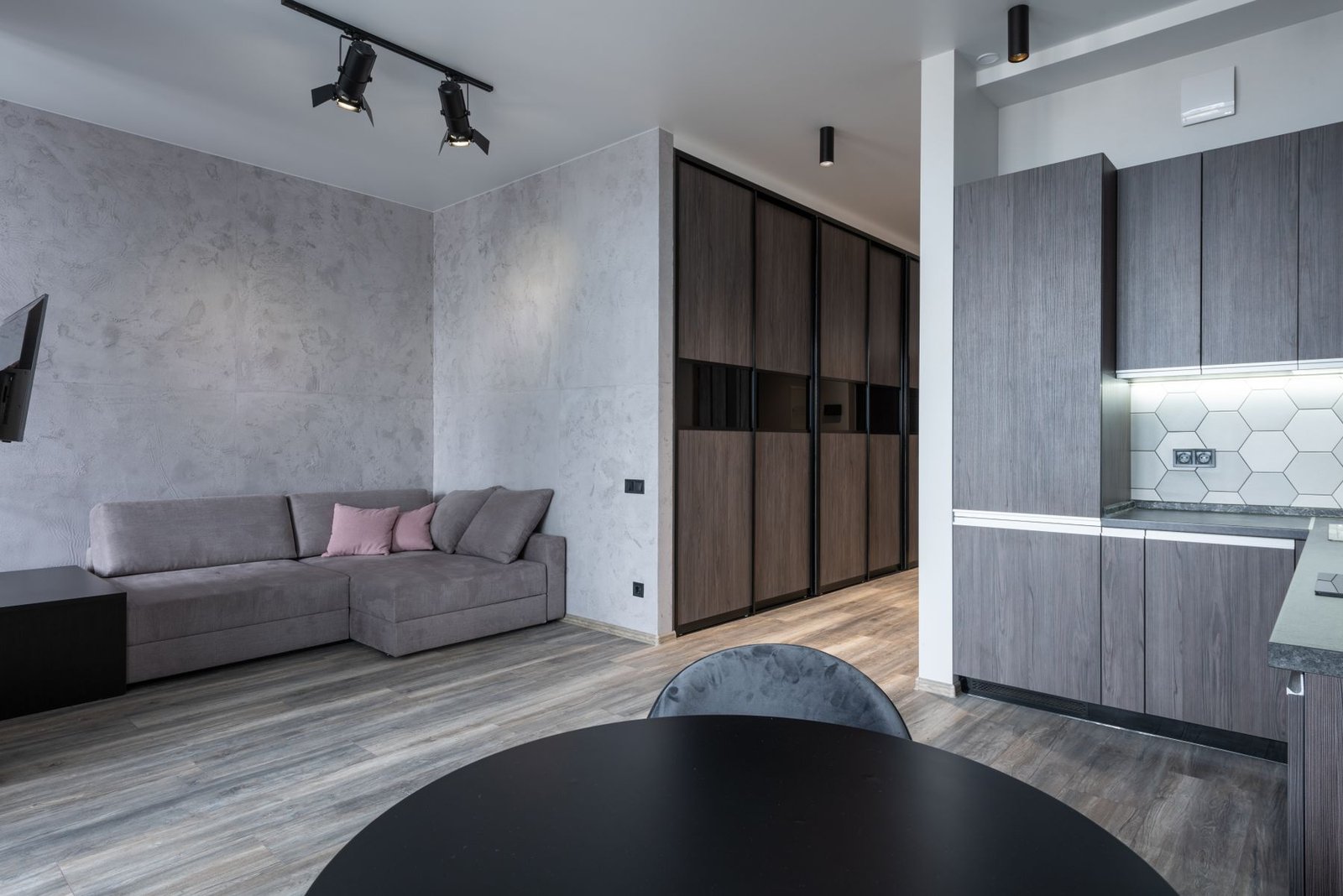 A compact apartment with a gray sofa, tall wood-fronted storage and a clear route beside the kitchen.